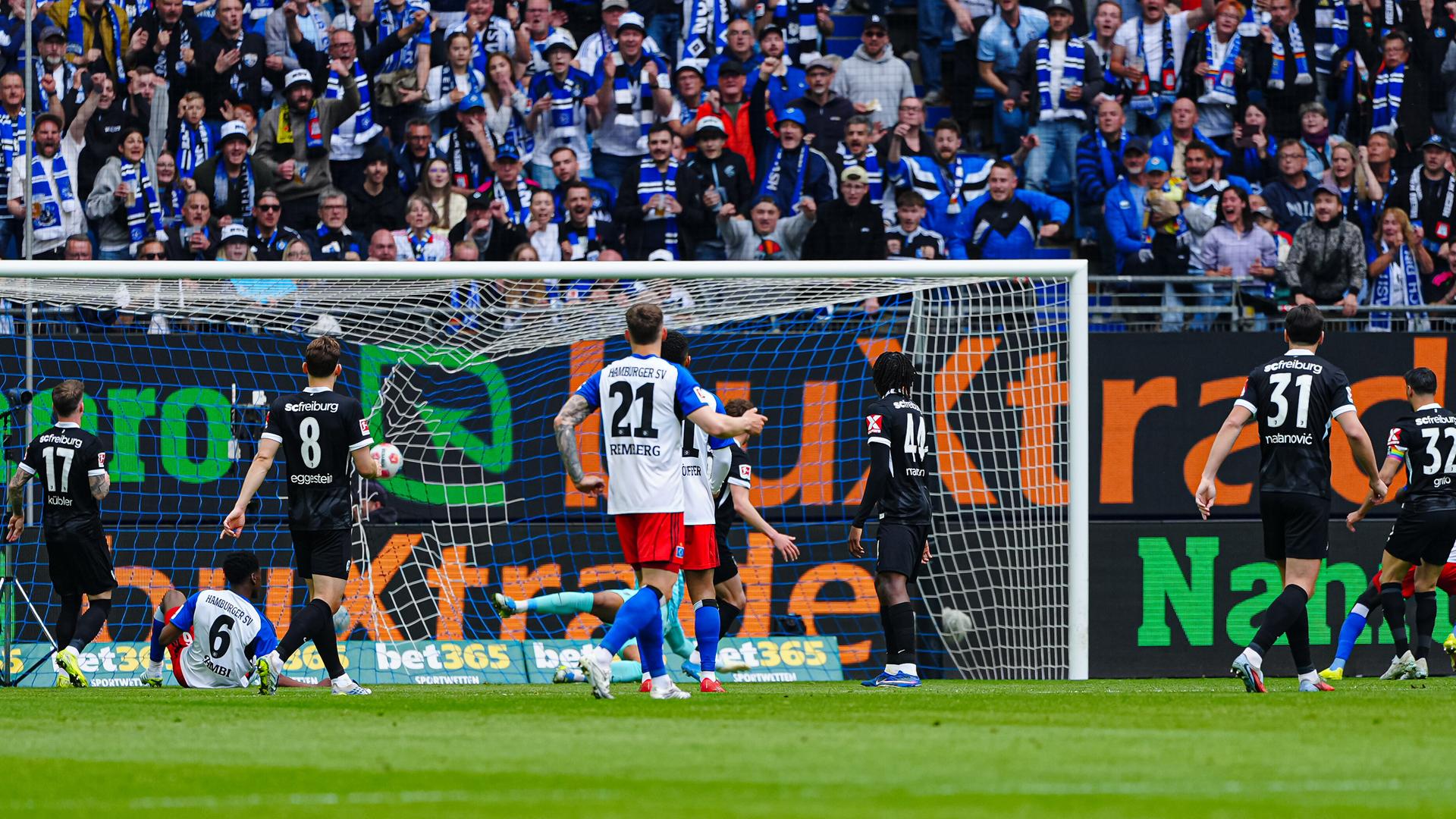 Fußball-Bundesliga: Spieler des HSV und des SC Freiburg vor einem Tor; der Ball fliegt durch die Luft.