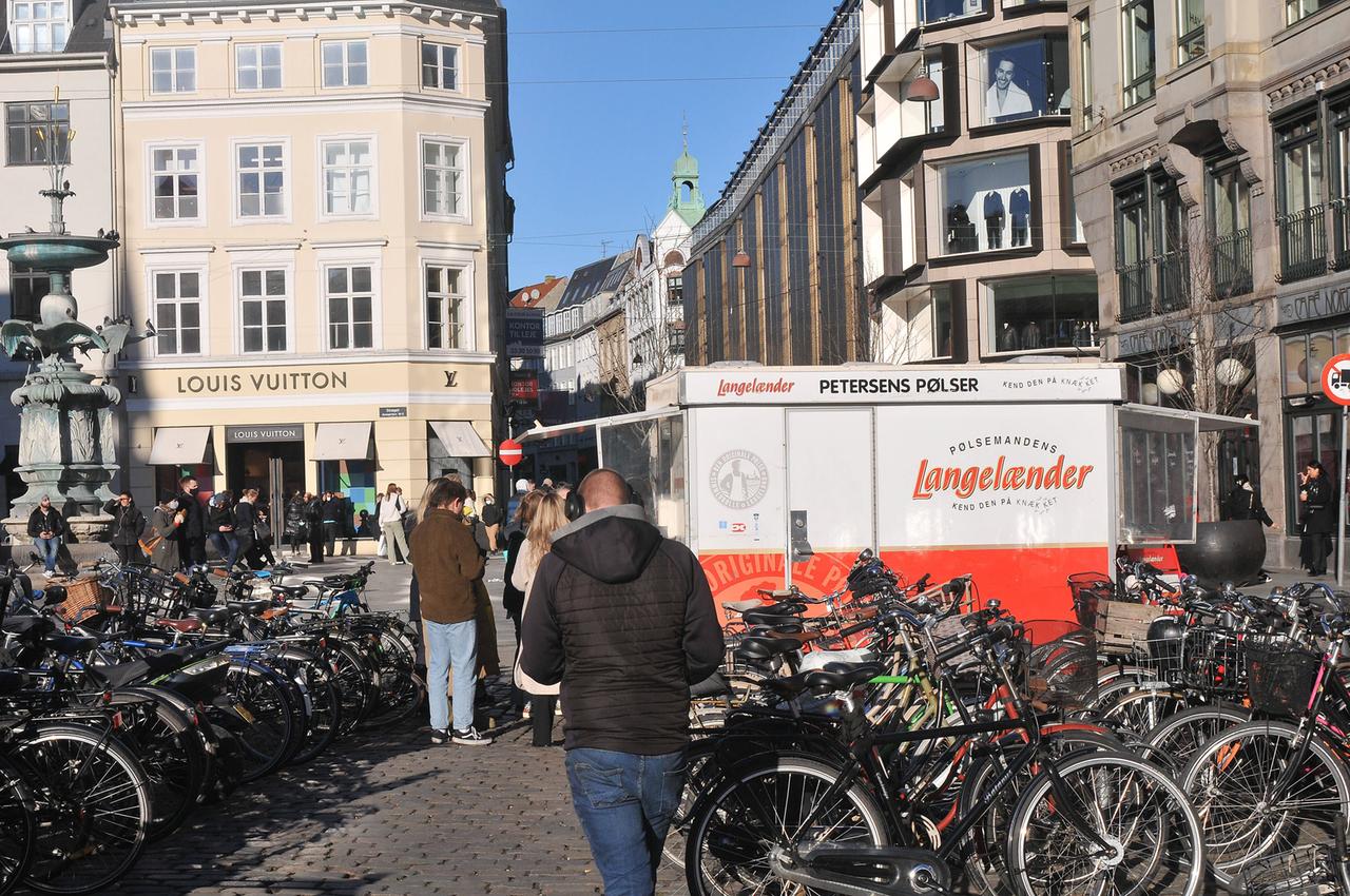 Menschen laufen in Kopenhagen auf einem Marktplatz, auf dem unzählige Fahrräder stehen.