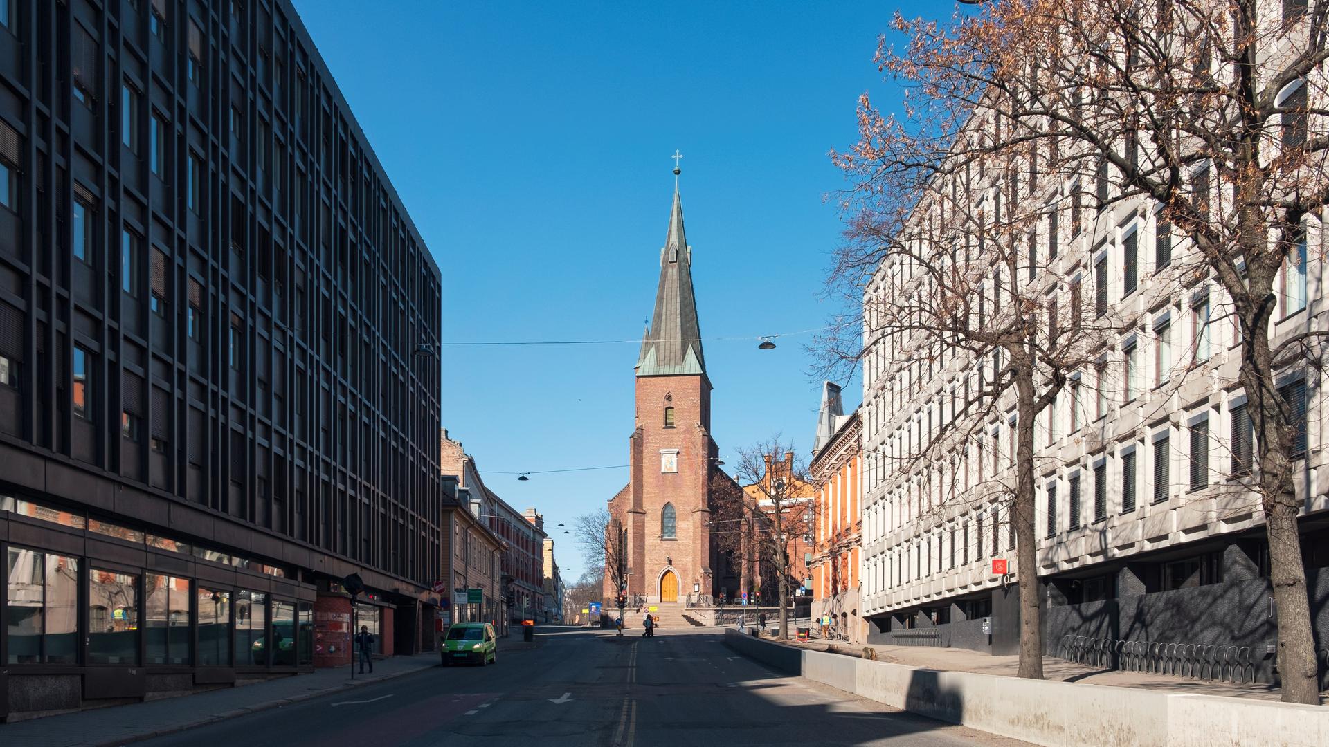 Straßenzug in Oslo, an dessen Ende eine von der Sonne beschienene Domkirche aus rotem Gestein steht.