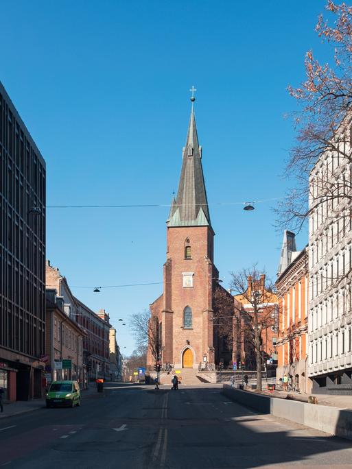 Straßenzug in Oslo, an dessen Ende eine von der Sonne beschienene Domkirche aus rotem Gestein steht.