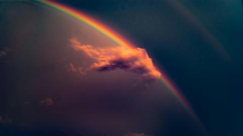 Blick auf eine Wolke am dunklen Himmel, die einen Regenbogen streift. 