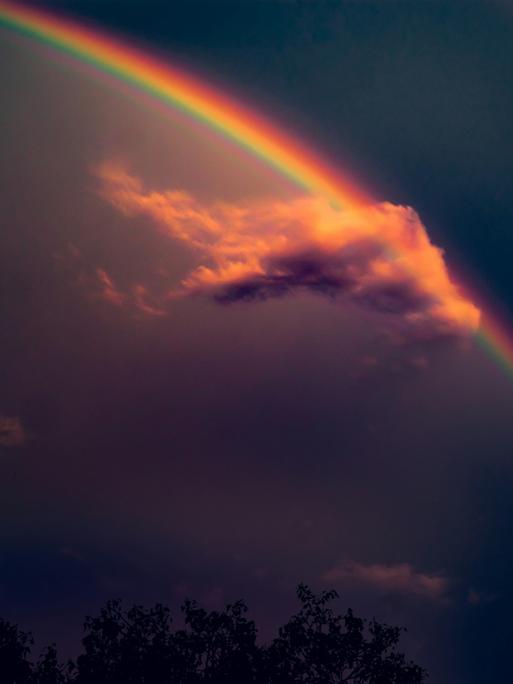 Blick auf eine Wolke am dunklen Himmel, die einen Regenbogen streift. 
