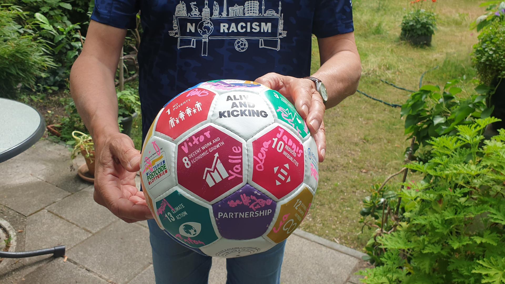 Oliver Brendle, Nachhaltigkeitsbeauftragter beim FC Internationale Berlin hält einen Fußball vor seinem Körper. Es ist nur seine Körpermitte zu sehen. 