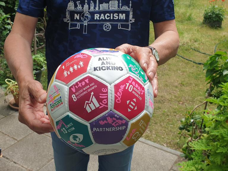 Oliver Brendle, Nachhaltigkeitsbeauftragter beim FC Internationale Berlin hält einen Fußball vor seinem Körper. Es ist nur seine Körpermitte zu sehen. 
