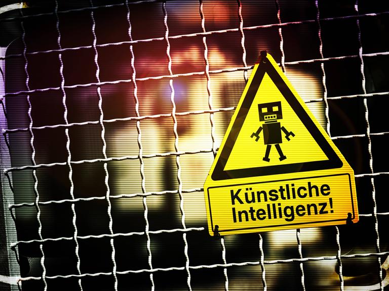 Die Fotomontage zeigt eine Roboterfigur auf einem Warnschild mit der Aufschrift "Künstliche Intelligenz". Das Schild hängt an einem Zaun.
