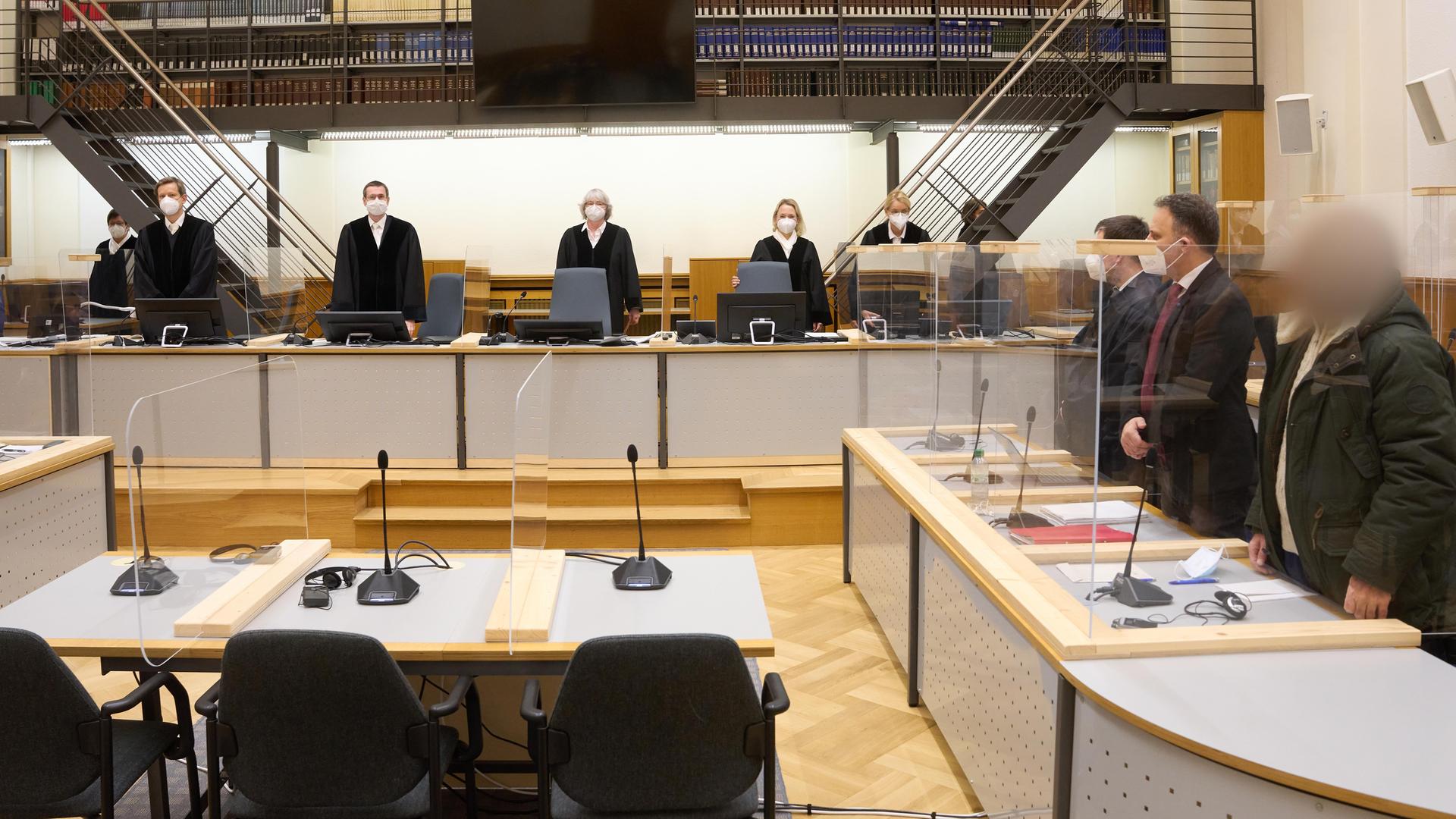 Prozess um Staatsfolter in Syrien. Der Angeklagte (r) und die anderen Prozessbeteiligten stehen im Gerichtssaal des Oberlandesgerichts.