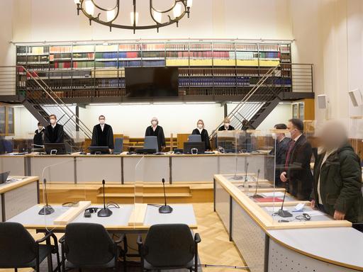 Prozess um Staatsfolter in Syrien. Der Angeklagte (r) und die anderen Prozessbeteiligten stehen im Gerichtssaal des Oberlandesgerichts.