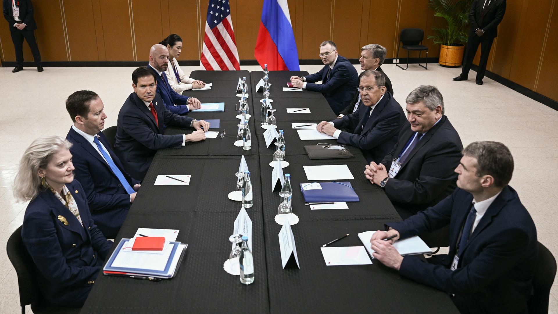 Die Außenminister der USA und Russlands, Rubio und Lawrow, sitzen sich mit ihren Mitarbeitern an einem langen Tisch gegenüber.