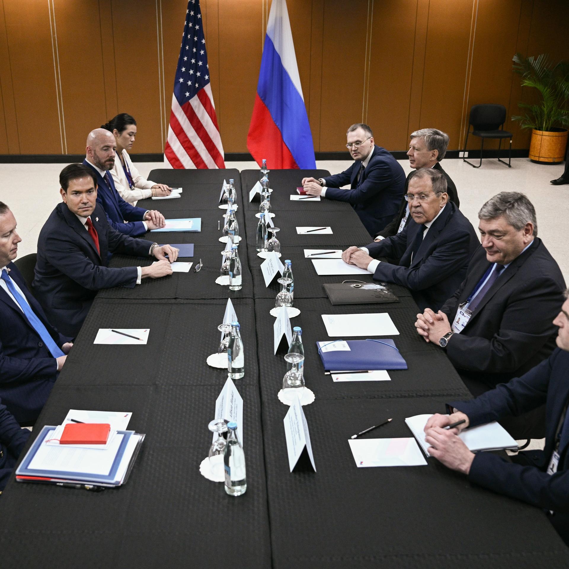 Die Außenminister der USA und Russlands, Rubio und Lawrow, sitzen sich mit ihren Mitarbeitern an einem langen Tisch gegenüber.