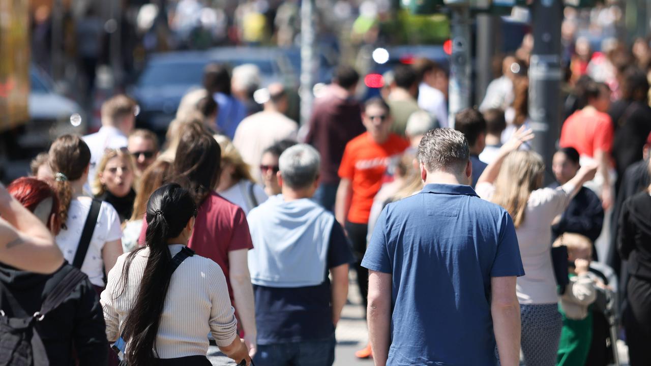 Zahlreiche Menschen gehen in einer Fußgängerzone nebeneinander.