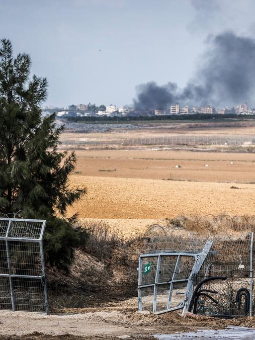 Blick auf ein zerstörtes Tor im Grenzzaun zwischen dem israelischen Kibbuz Kfar Aza und dem Gazastreifen. Im Hintergrund eine Rauchsäule.