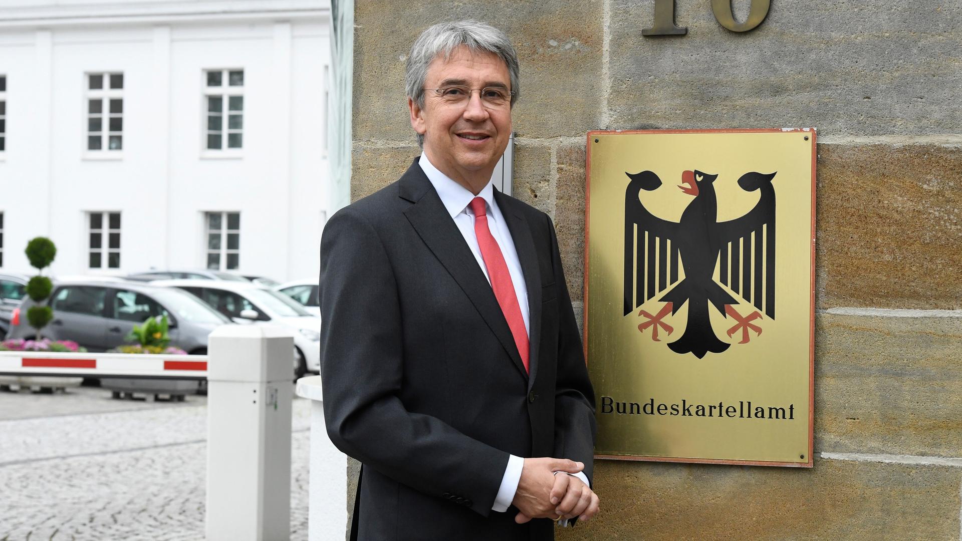 Andreas Mundt ist Präsident des Bundeskartellamtes. Er steht vor dem Sitz seiner Behörde und einem Schild mit Bundesadler. Andreas Mundt ist Präsident des Bundeskartellamtes. Er steht vor dem Sitz seiner Behörde und einem Schild mit Bundesadler.