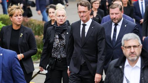 Die Politiker laufen nebeneinander mit weiteren Gästen der Gedenkfeier über einen Platz.