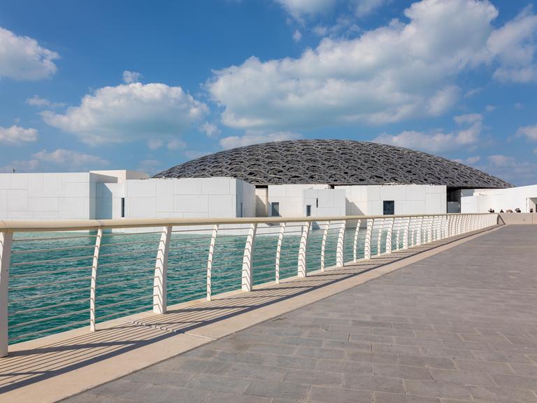 Das Kunstmuseum Louvre mit einem hochmodernen Bau in Abu Dhabi, zu dem eine Brücke am Meer führt