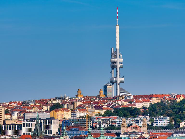 Ein zweiteiliger Fernsehturm ragt weit über die umgebenden Gebäude hinaus und hebt sich vor einem wolkenlosen Himmel ab.