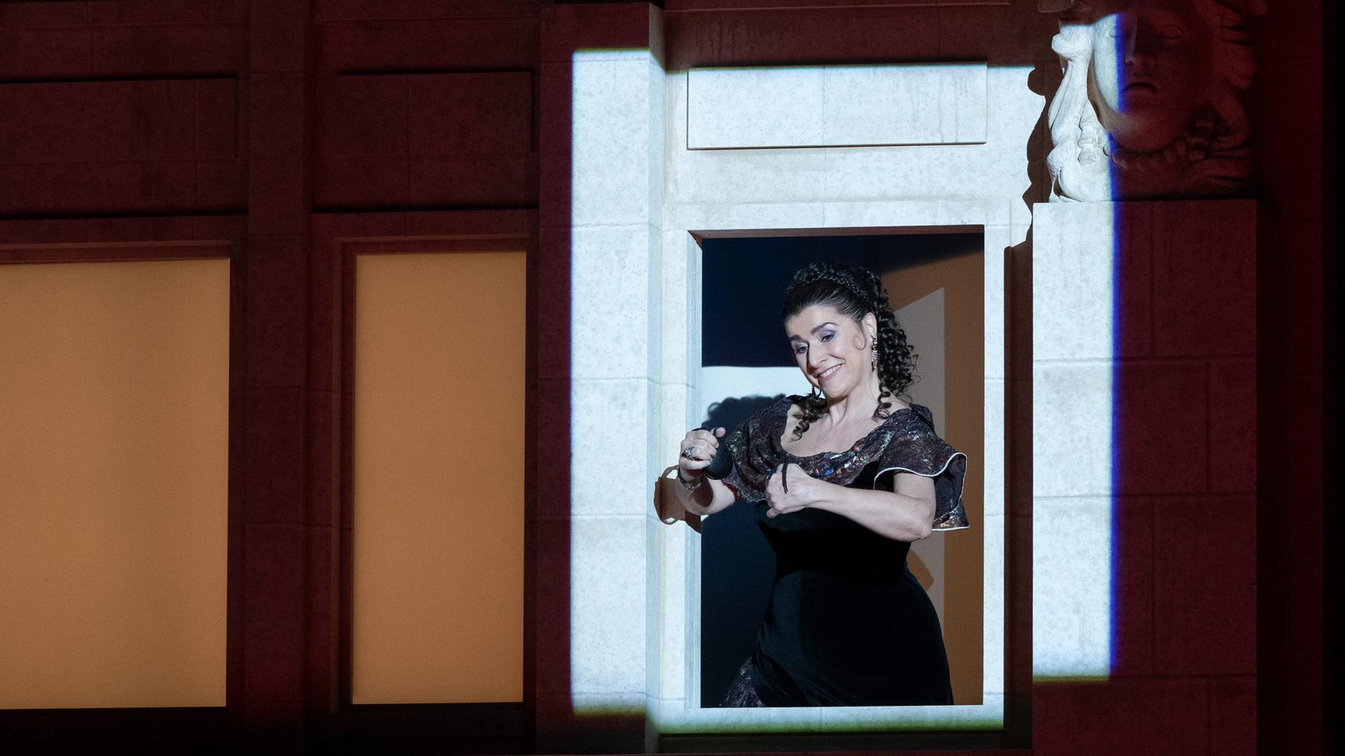 Cecilia Bartoli steht an einem beleuchteten Fenster und spielt Kastanietten.