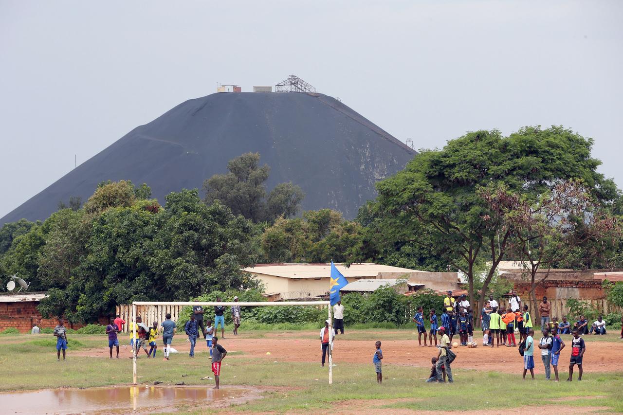 Ein belebter Fußballplatz mit spielenden Kindern in Lubumbashi, Kongo. Im Hintergrund ist eine große Mine zu sehen. Lubumbashi ist die Bergbauhauptstadt der Demokratischen Republik Kongo und fungiert als Drehscheibe für viele der größten Bergbauunternehmen des Landes.