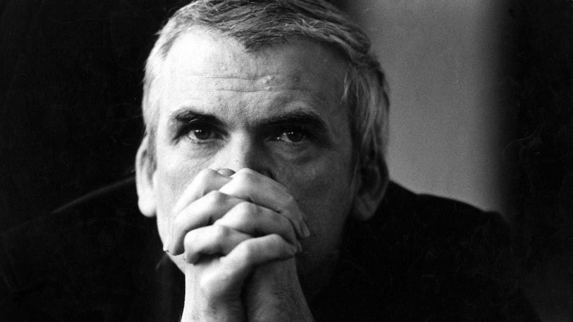Der tschechische Schriftsteller Milan Kundera schaut über seine gefalteten Hände in die Kamera. Die Schwarz-Weiß-Aufnahme stammt aus dem Jahr 1981.