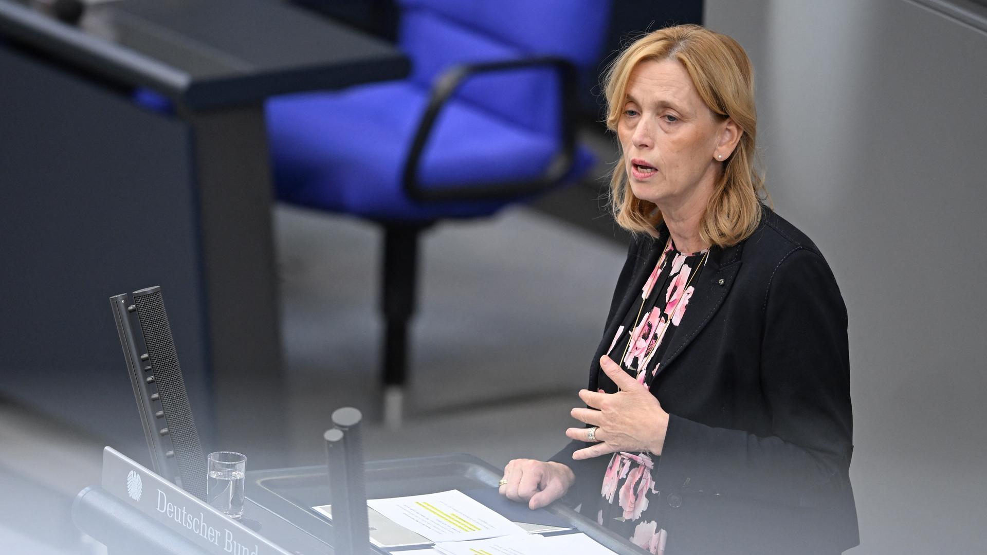 Prien steht am Rednerpult und spricht. Sie gestikuliert dazu mit der linken Hand. Sie trägt ein geblümtes Kleid und ein schwarzes Jackett. Prien steht am Rednerpult und spricht. Sie gestikuliert dazu mit der linken Hand. Sie trägt ein geblümtes Kleid und ein schwarzes Jackett.