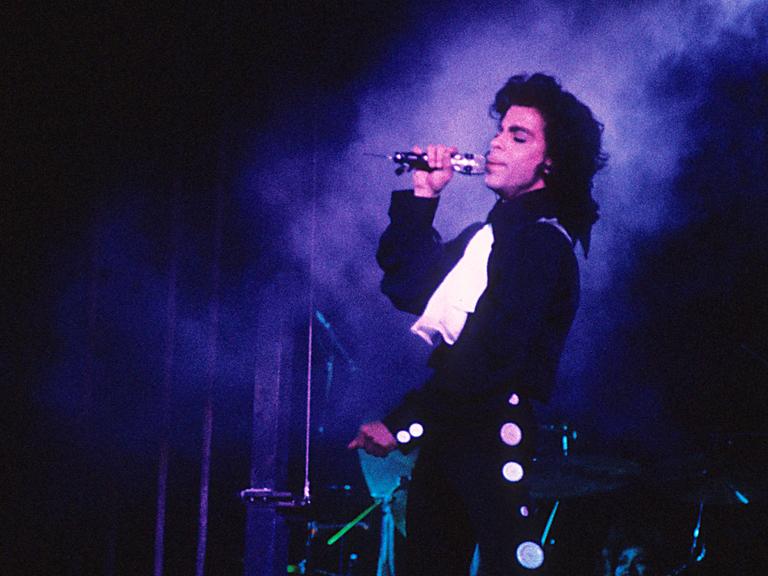 Prince singt auf der Bühne in purpurem Licht. Prince singt auf der Bühne in purpurem Licht.