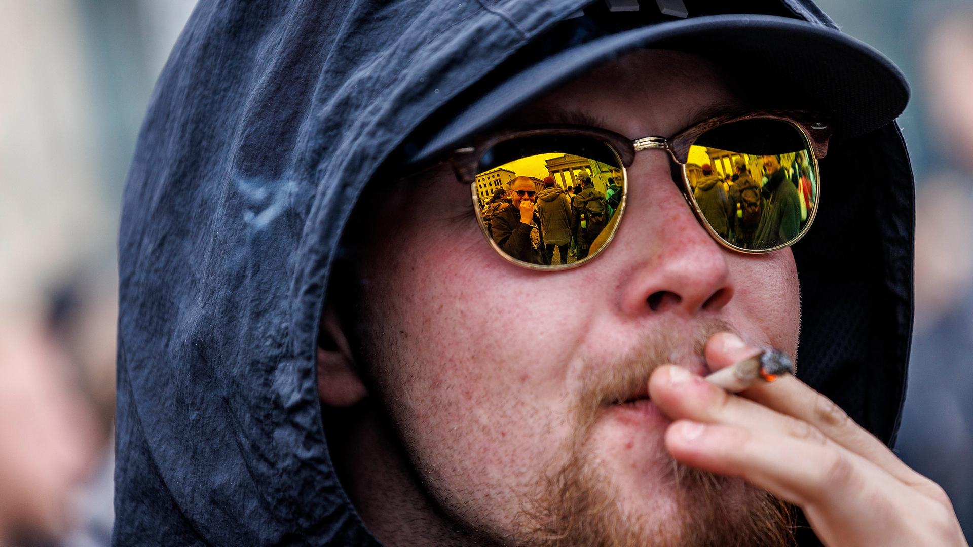 Ein Mann mit goldverspiegelter Brille raucht einen Joint. Ein Mann mit goldverspiegelter Brille raucht einen Joint.