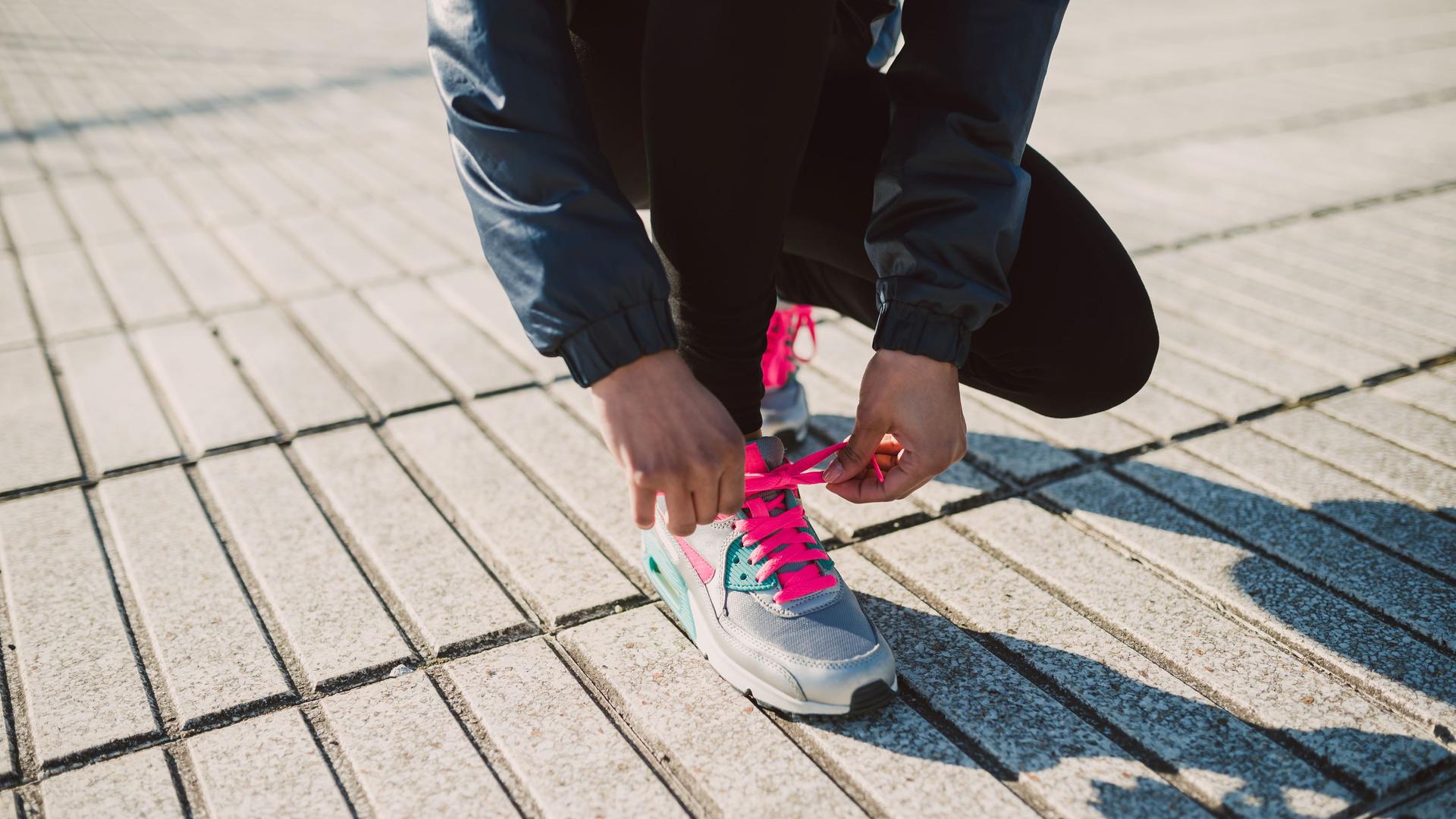 Eine Frau bindet sich vor dem Joggen die Joggingschuhe zu.