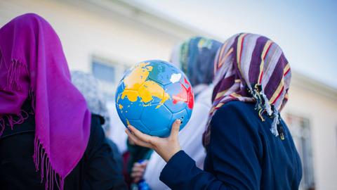 Ein syrisches Mädchen mit Kopftuch hält in einem Flüchtlingscamp einen Fussball in Form einer Weltkugel in den Händen.