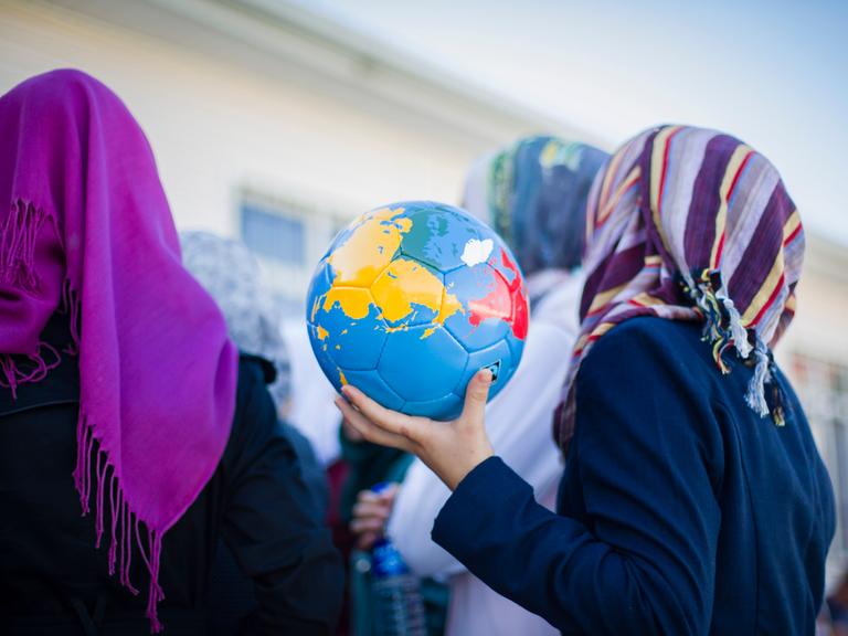Ein syrisches Mädchen mit Kopftuch hält in einem Flüchtlingscamp einen Fussball in Form einer Weltkugel in den Händen.