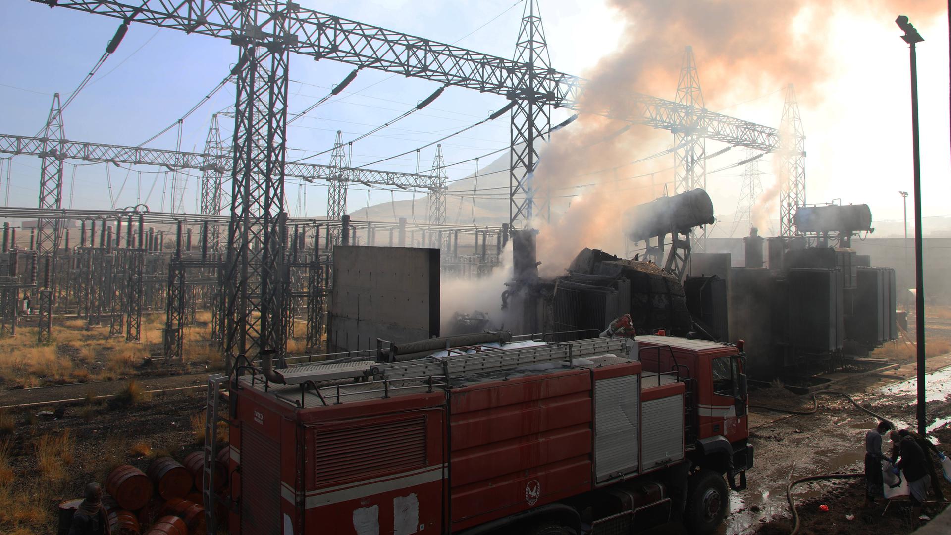 Aus einer Umspannanlage dringt dichter Rauch. Davor steht ein Eisenbahnwaggon. Darüber blauer Himmel.