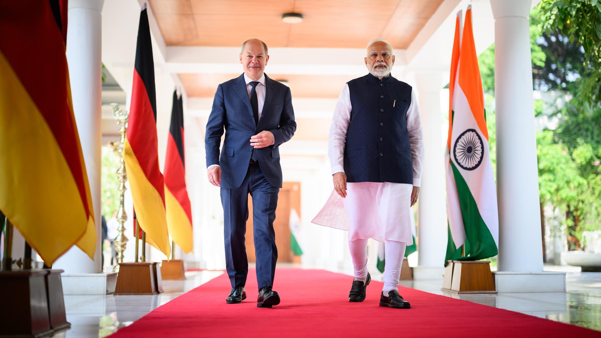 Bundeskanzler Olaf Scholz (SPD und der indische Premierminister Narendra Modi laufen bei den 7. Deutsch-Indischen Regierungskonsultationen zusammen über einen roten Teppich einen Gang entlang, der mit Fahnen beider Länder geschmückt ist. 