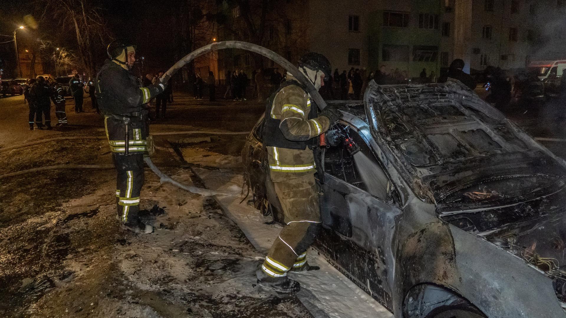 Rettungskräfte löschen bei Nacht einen Brand in einem Wohngebiet voller Trümmer. 
