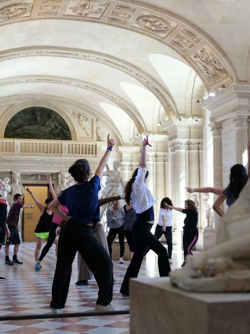Menschen tanzen zwischen antiken Skulpturen auf Marmorboden im Caryatides Raum des Louvre.