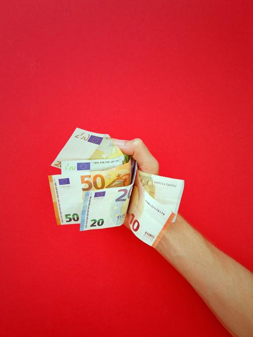 Mehrere Geldscheine werden von einer Hand gehalten. Der Hintergrund ist rot.