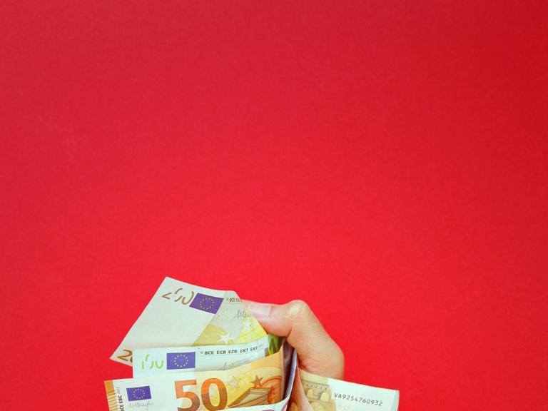 Mehrere Geldscheine werden von einer Hand gehalten. Der Hintergrund ist rot.