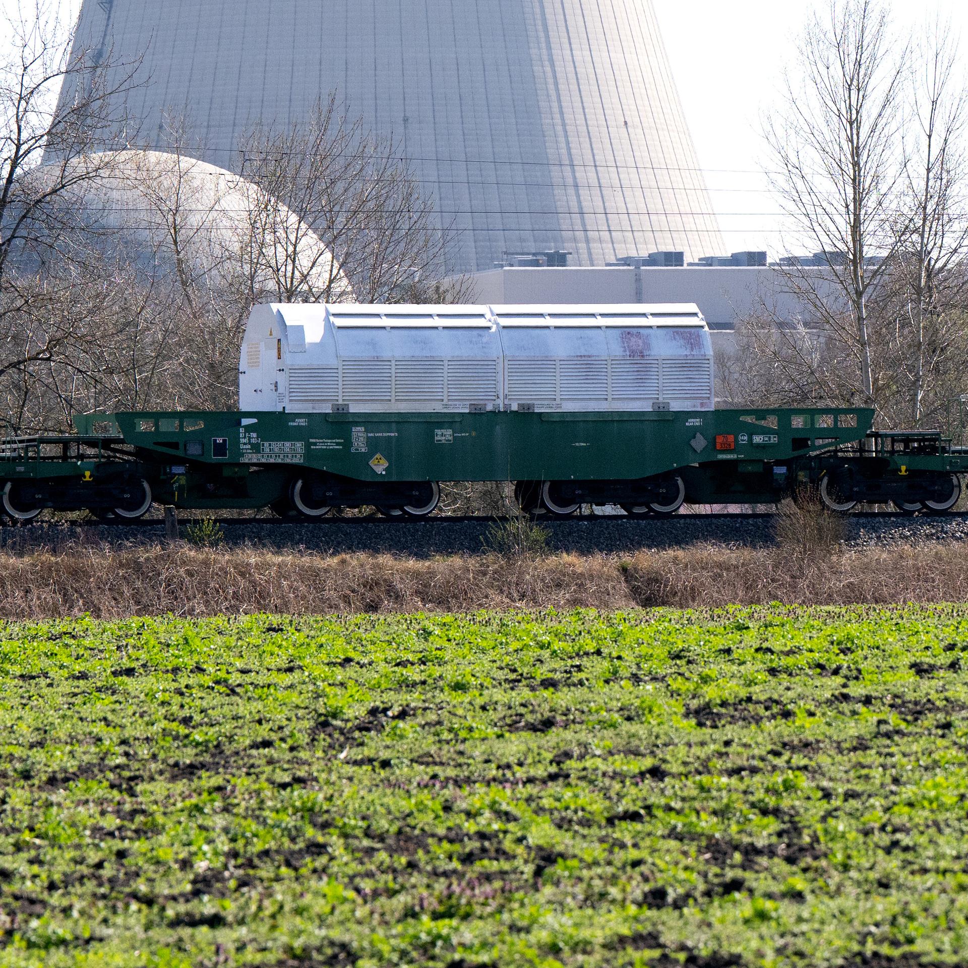 Ein grauer Castor-Behälter steht auf einem Waggon. Dahinter ist ein Kraftwerk zu sehen.