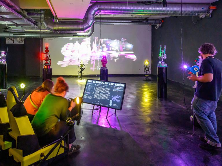 Besucherinnen der Ars Electronica sitzen in einem abgedunkelten Raum vor einem Bildschirm.