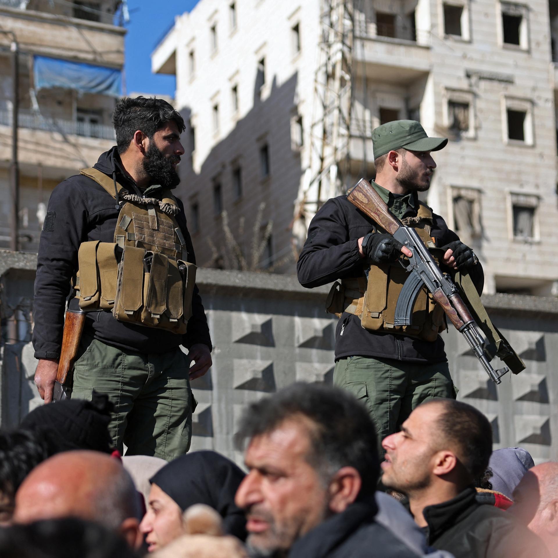 Zwei bewaffnete Soldaten stehen erhöht neben einem Strom von Menschen auf der Straße.