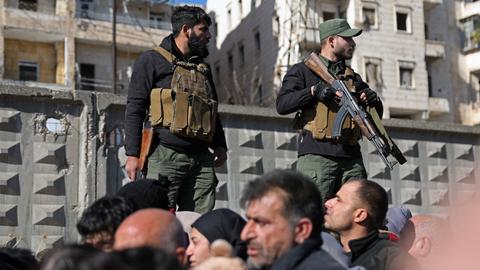 Zwei bewaffnete Soldaten stehen erhöht neben einem Strom von Menschen auf der Straße.