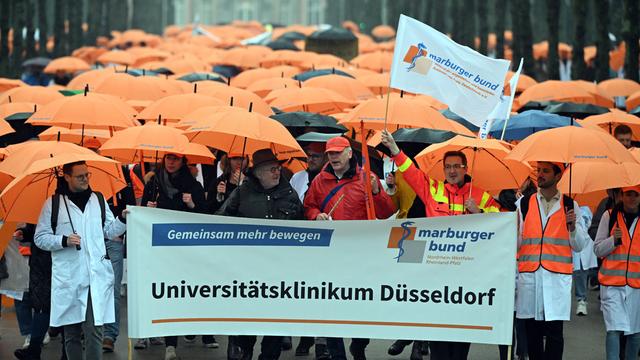 Ärztinnen und Ärzte protestieren in Düsseldorf. Viele Personen mit Regenschirmen stehen hintereinander.