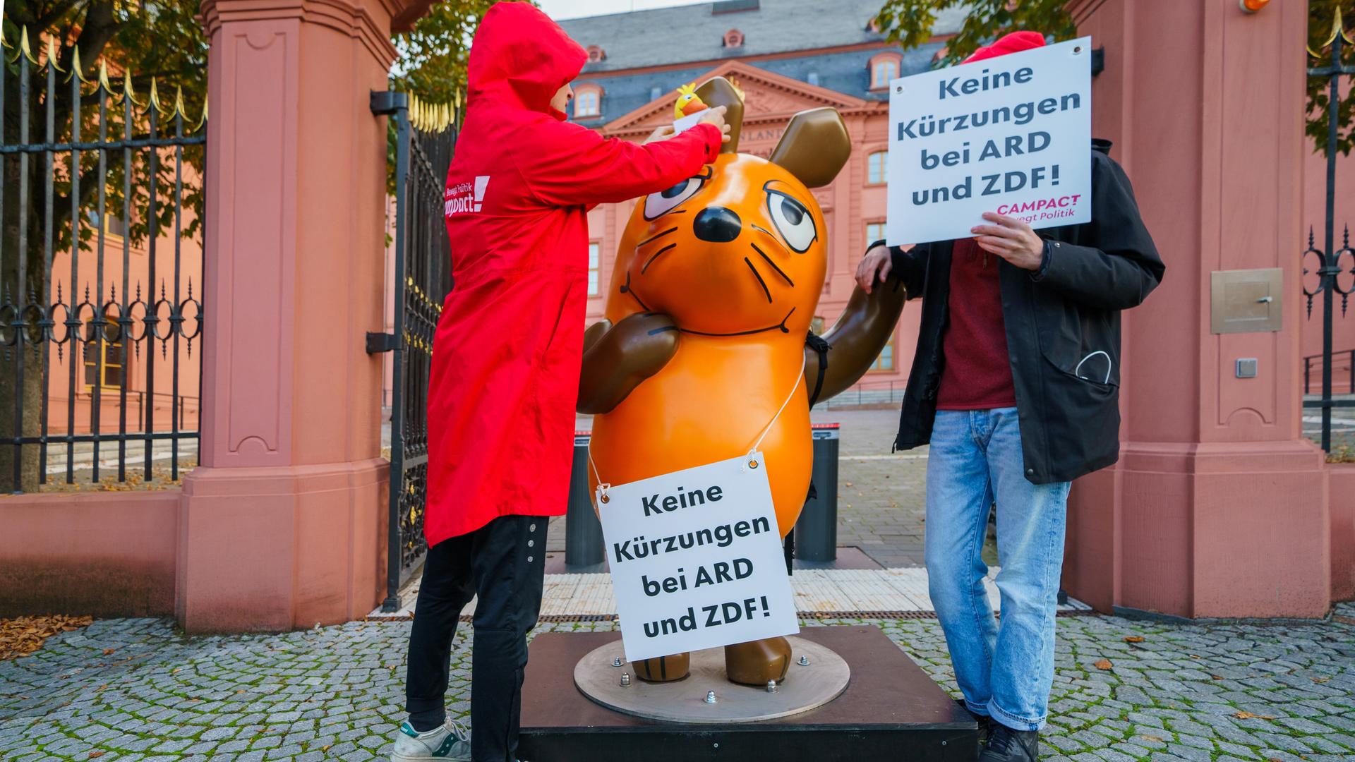 Mainz: Die Figur der Maus aus der "Sendung mit der Maus" steht zwischen Aktivisten von Campact vor dem Landtag Rheinland-Pfalz, die Schilder mit der Aufschrift "Keine Kürzungen bei ARD und ZDF!" halten. 