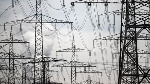 Zahlreiche Strommasten stehen auf einem Acker, dahinter ein grau-bewölkter Himmel.