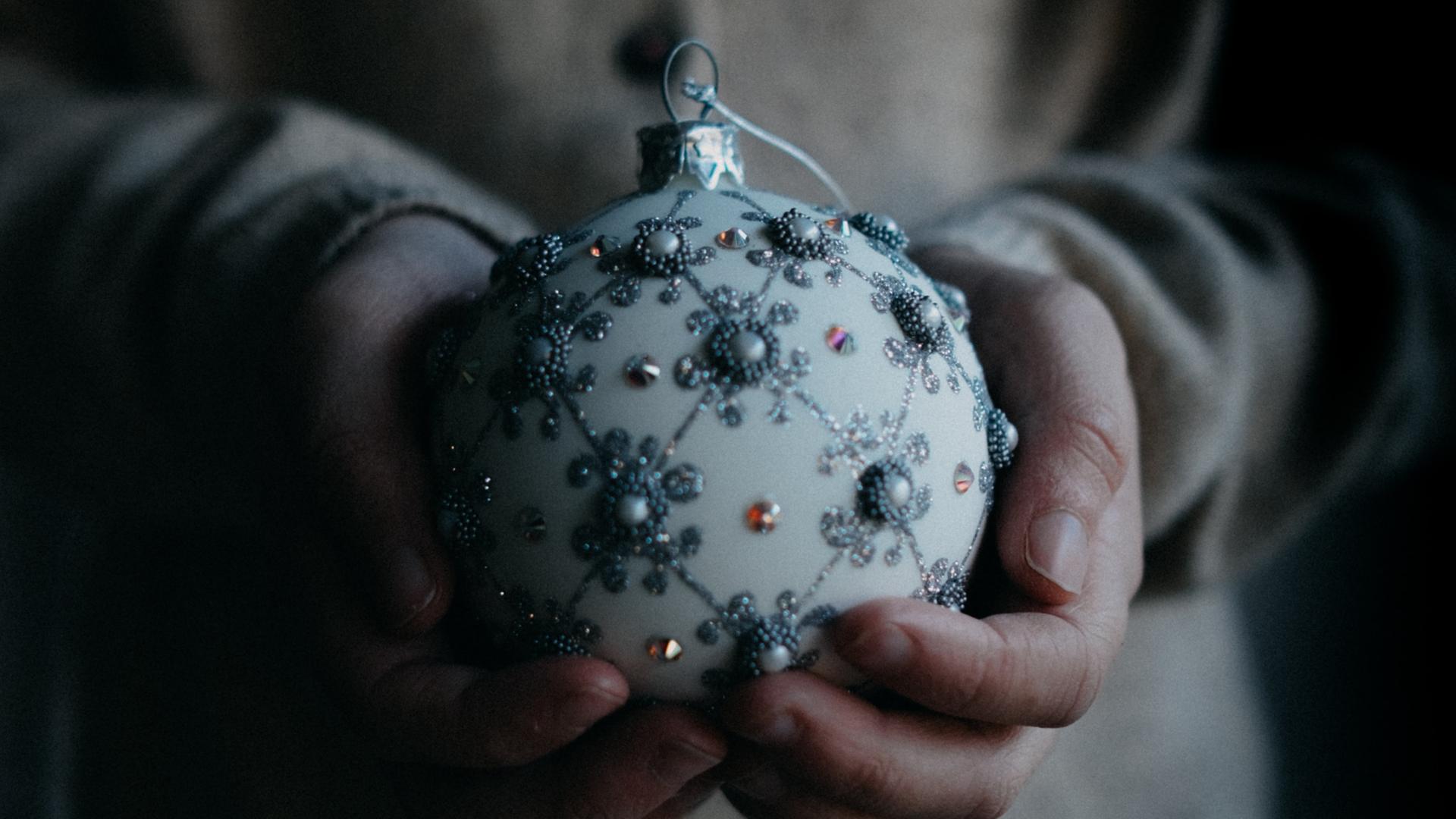 Eine mit Perlen geschmückte Weihnachtskugel liegt in den Händen einer jungen Frau.