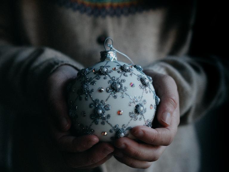 Eine mit Perlen geschmückte Weihnachtskugel liegt in den Händen einer jungen Frau.
