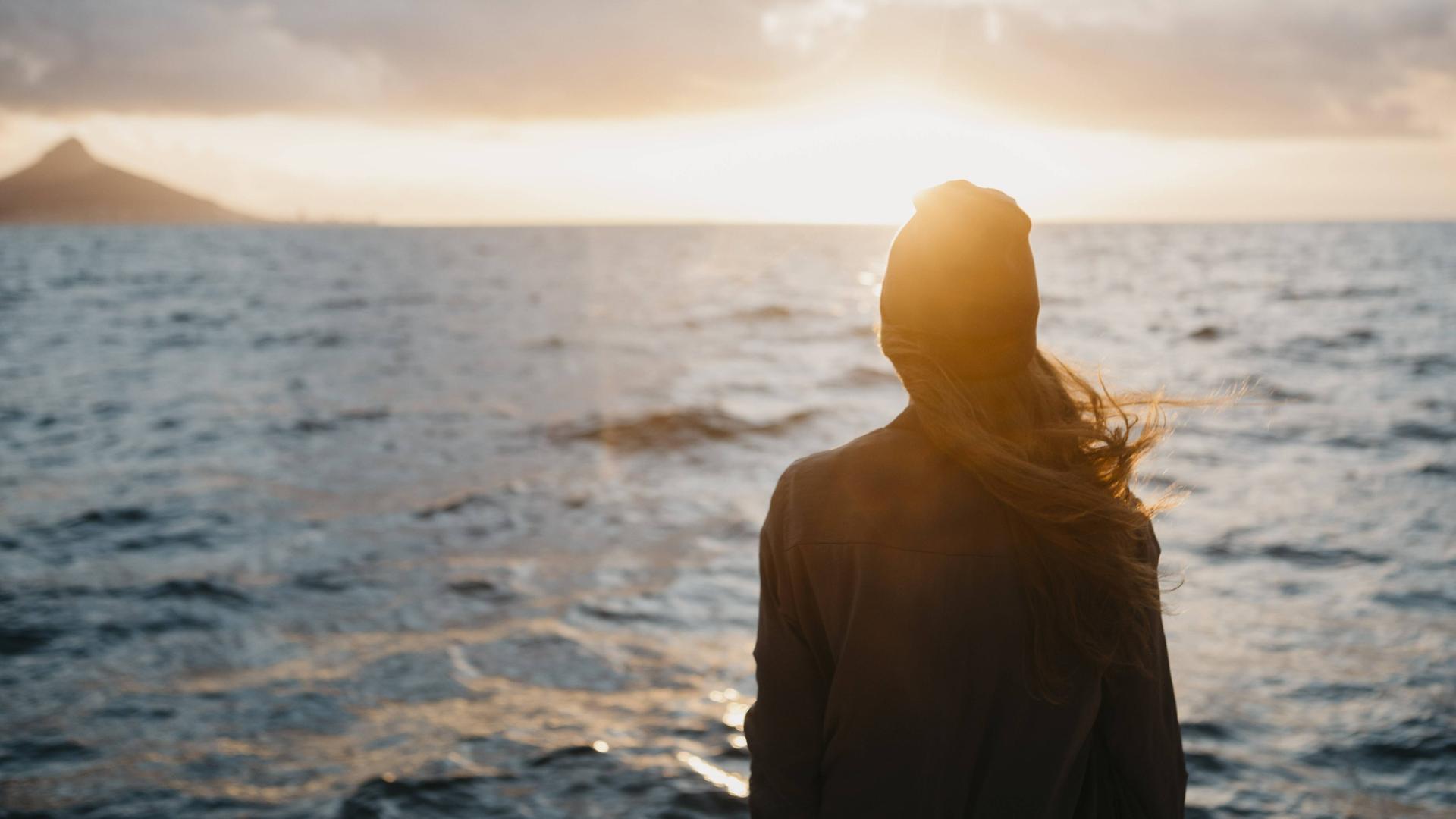 Eine junge Frau blickt auf den Meereshorizont bei Sonnenuntergang.
