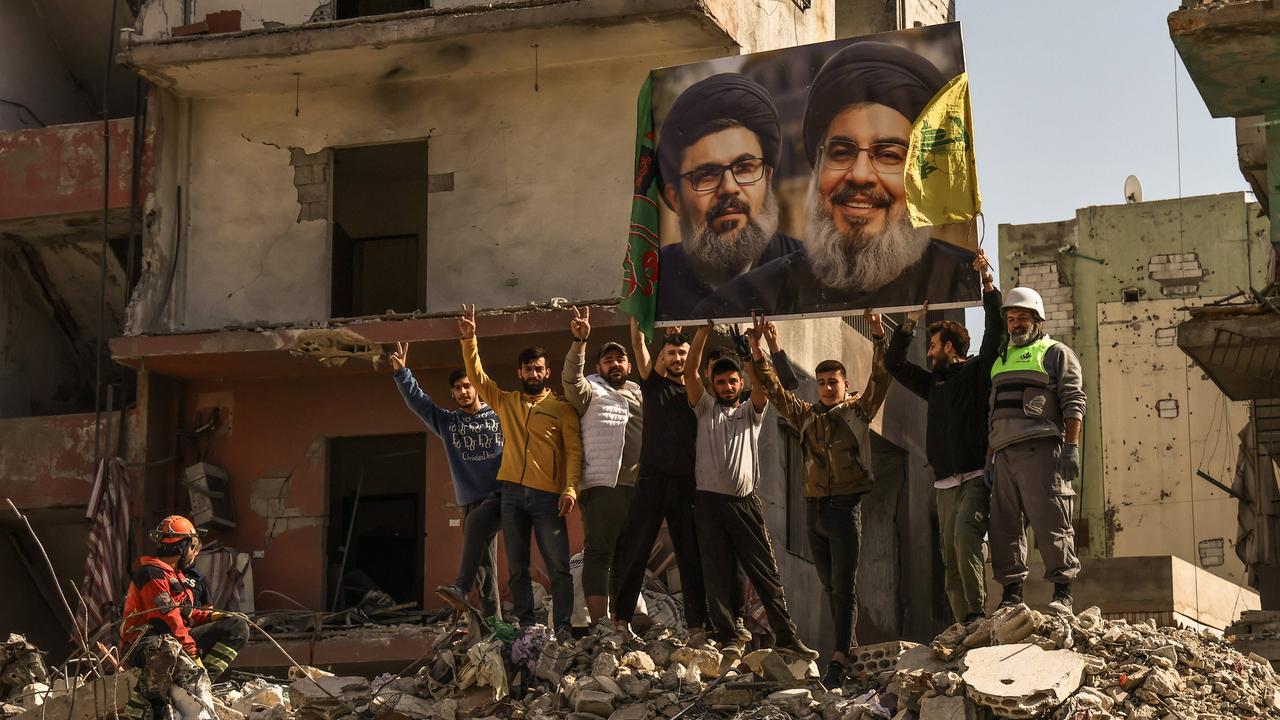 Menschen in dem von der Hisbollah kontrollierten Dahieh Viertel im Süden Beiruts in Trümmern halten ein Foto eines Politikers mit schwarzem Turban  hoch