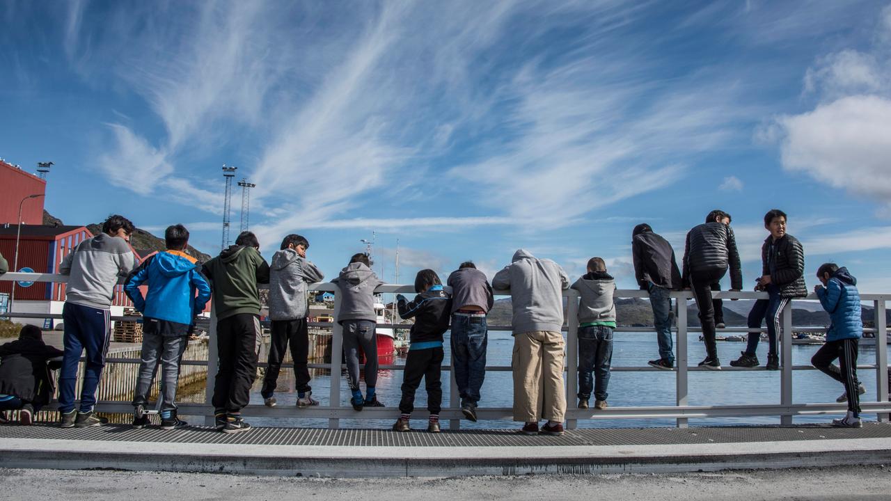 Eine Gruppe jugendlicher Jungs steht an einer hölzernen Uferbegrenzung. Manche sind daran gelehnt und schauen aufs Wasser, andere sitzen rittlings darauf.