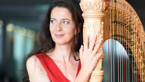 Silke Aichhorn steht in einem roten Kleid neben ihrer Harfe.