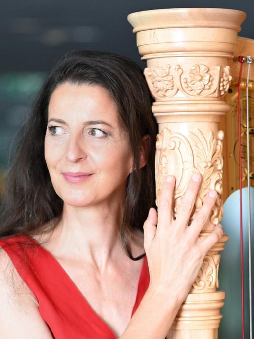Silke Aichhorn steht in einem roten Kleid neben ihrer Harfe.