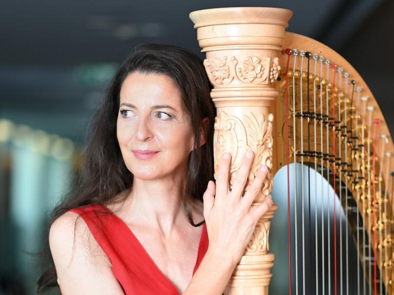 Silke Aichhorn steht in einem roten Kleid neben ihrer Harfe.