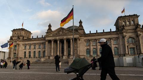Vor dem Reichstag in Berlin, dem Sitz des Deutschen Bundestages, flanieren Menschen.